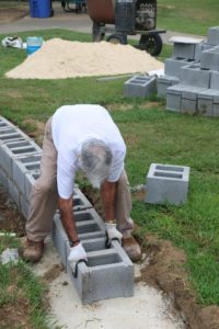 Veteran Gerald Dukes braved the heat to help lay some 12 inch blocks. (Photo by Kayron Duffey)